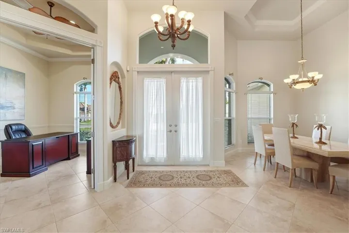 Foyer entrance with a chandelier, french doors, crown molding, a towering ceiling, and light tile patterned flooring
