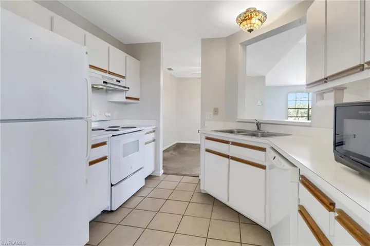 Kitchen with white cabinets, a sink, light countertops, white appliances, and under cabinet range hood