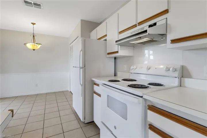 Kitchen featuring light countertops, white cabinetry, a wainscoted wall, under cabinet range hood, and white electric range