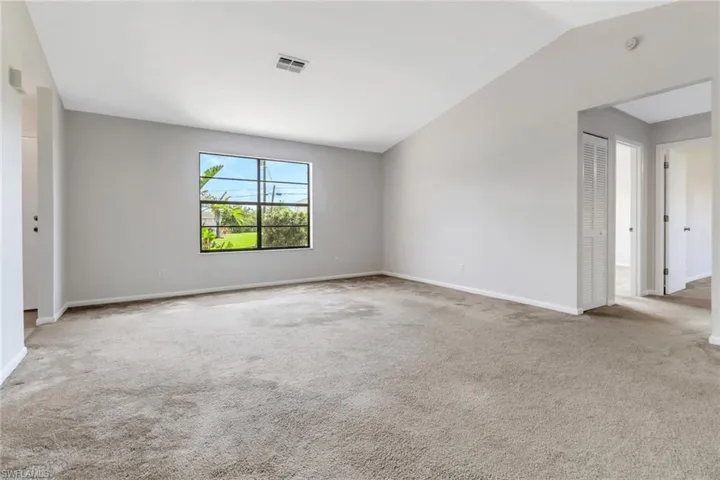 Carpeted spare room with visible vents, baseboards, and lofted ceiling