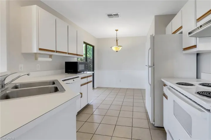 Kitchen featuring white appliances, white cabinetry, under cabinet range hood, visible vents, and a sink