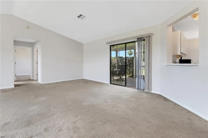 Carpeted empty room featuring baseboards, vaulted ceiling, and visible vents