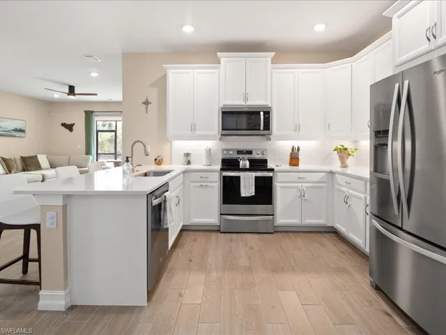 Kitchen with sink, kitchen peninsula, light hardwood / wood-style floors, a breakfast bar, and appliances with stainless steel finishes