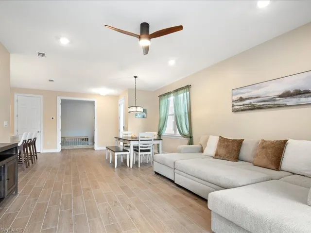 Living room with ceiling fan with notable chandelier and light hardwood / wood-style flooring