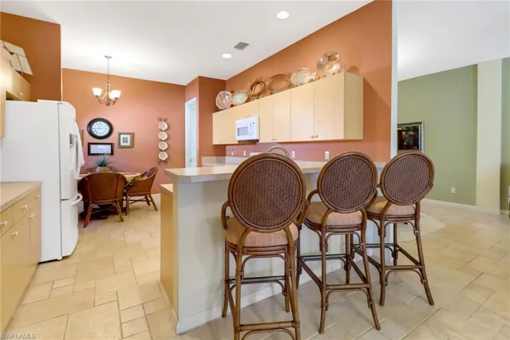 Kitchen featuring kitchen peninsula, a kitchen breakfast bar, white appliances, decorative light fixtures, and a notable chandelier