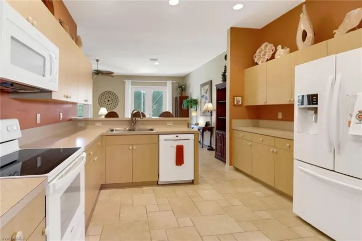 Kitchen with ceiling fan, sink, kitchen peninsula, white appliances, and light brown cabinetry