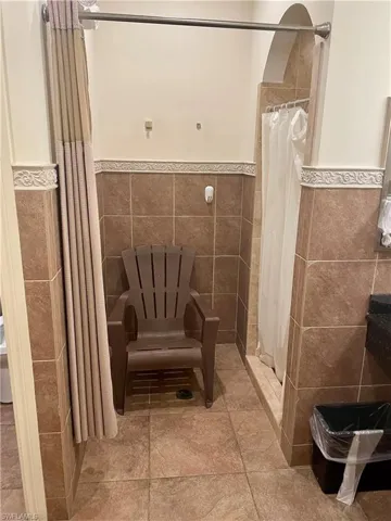 Bathroom featuring a tile shower, wainscoting, and tile walls