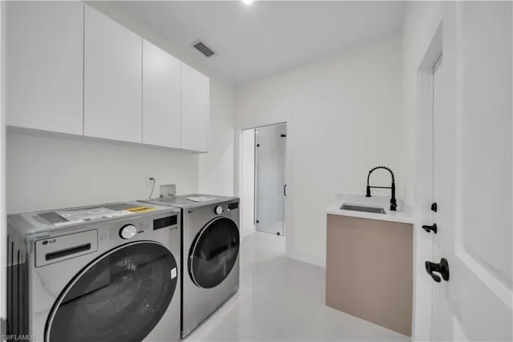 Utility room with white shaker-style cabinetry, a built-in sink with a matte black faucet, and light-toned tile flooring