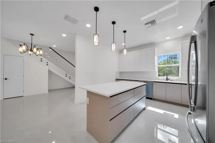 Sleek kitchen featuring a central island with countertop space and integrated drawers, white flat-panel cabinetry, stainless steel appliances, and a black gooseneck faucet