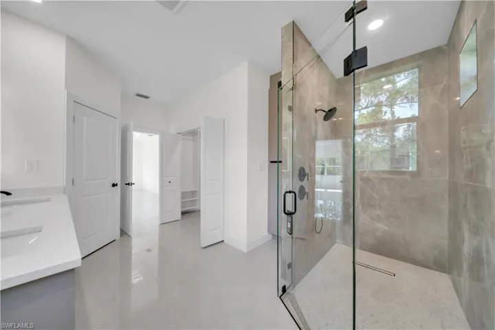Spacious master shower  featuring a glass-enclosed area with tiled walls , dual vanity with undermount sinks and quartz countertops, and light-toned floor tiling