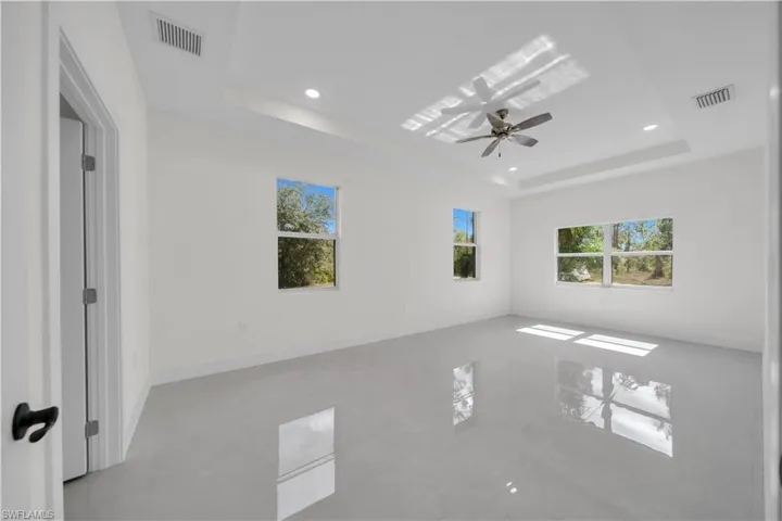Master bedroom with light-toned tile flooring, a tray ceiling with recessed lighting, and a ceiling fan