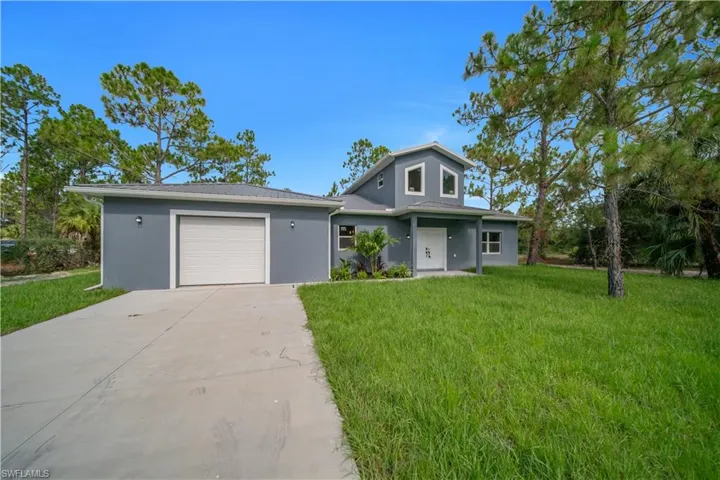 Contemporary home exterior featuring a two-story elevation, attached single-car garage, white garage door, concrete driveway, and a front lawn with mature trees