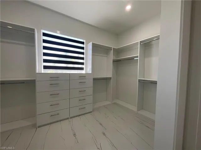 Well-appointed closet space featuring built-in shelving, hanging rods, and a window with blinds