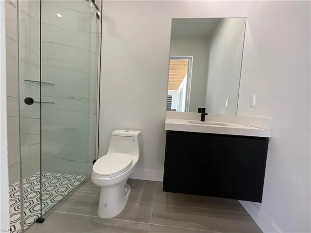 Bathroom featuring a glass-enclosed shower with patterned floor tiles, a modern floating vanity with a white countertop, and a large wall-mounted mirror