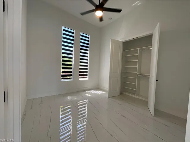Room featuring two vertical windows with blinds, a ceiling fan with light, and light-toned flooring