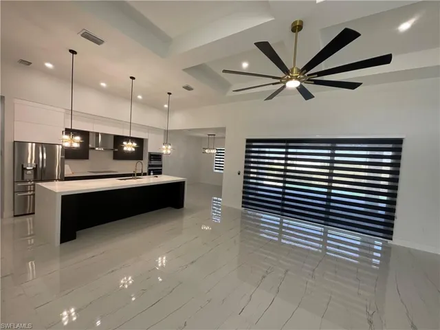 Contemporary kitchen and living area featuring sleek white tile flooring, a large kitchen island with white countertop, stainless steel refrigerator, and recessed lighting