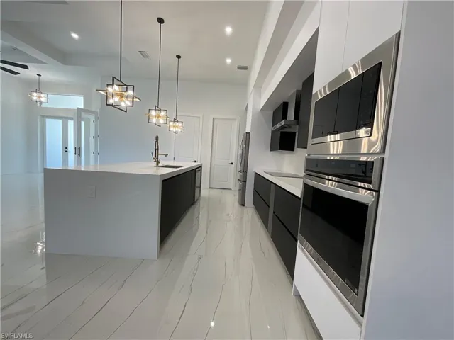 The kitchen features a large island with a sink and modern pendant lighting, sleek white and black cabinetry, built-in stainless steel appliances, and polished tile flooring