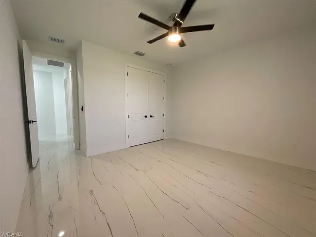 This room features white walls, white tile flooring with dark veining, a white door with a black handle, and a ceiling fan with integrated lighting