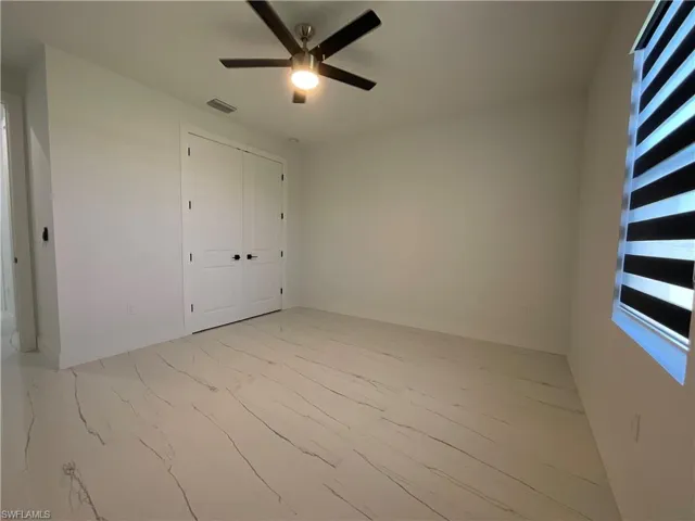 This room features clean white walls, a ceiling fan with integrated lighting, and a large window with horizontal blinds