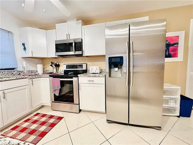 Kitchen featuring stainless steel appliances, white cabinets, light tile patterned floors, and light stone counters