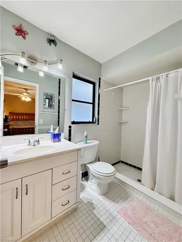 Ensuite bathroom featuring vanity, a stall shower, light tile patterned flooring, and a ceiling fan