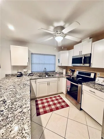 Kitchen featuring stainless steel appliances, light stone counters, white cabinetry, light tile patterned floors, and ceiling fan