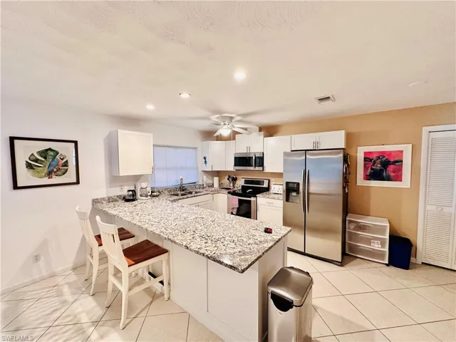 Kitchen with appliances with stainless steel finishes, light tile patterned floors, light stone counters, white cabinets, and a kitchen breakfast bar