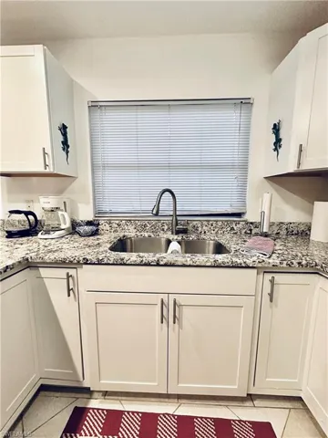 Kitchen with light tile patterned floors, light stone countertops, and white cabinetry