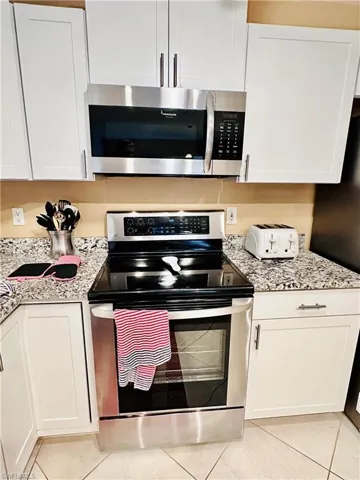 Kitchen featuring appliances with stainless steel finishes, light tile patterned flooring, white cabinetry, and light stone counters