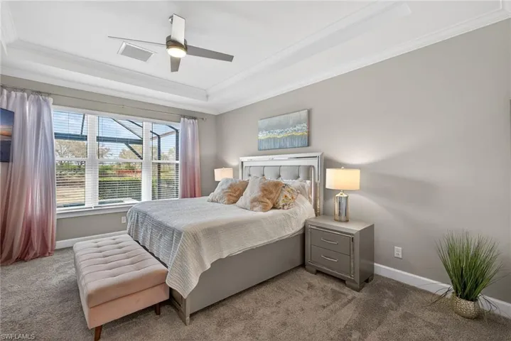 Primary bedroom. Carpeted bedroom with ornamental molding, ceiling fan, and a tray ceiling