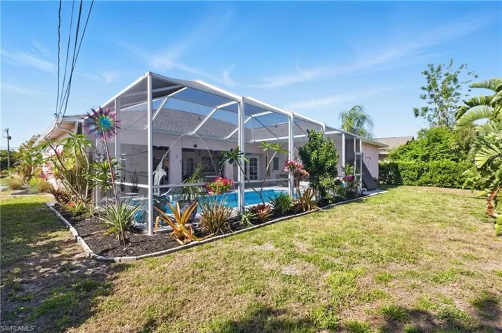 Back of property featuring a yard, an outdoor pool, and glass enclosure
