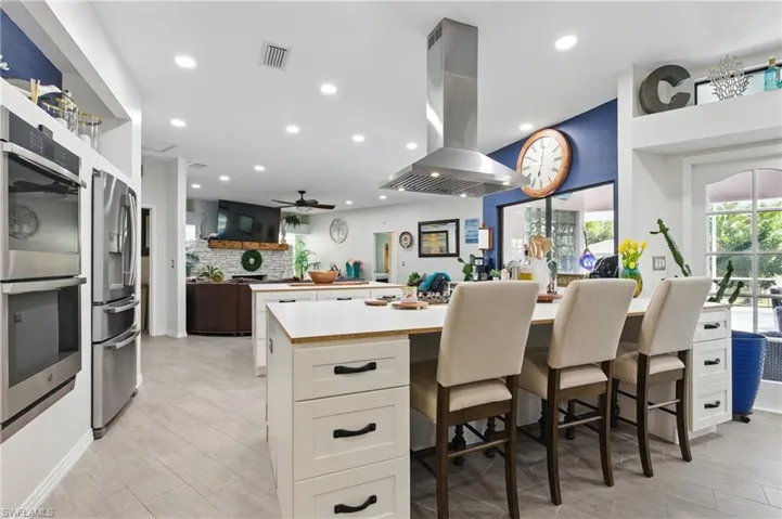 Kitchen featuring tasteful backsplash, light countertops, white cabinets, visible vents, and island range hood