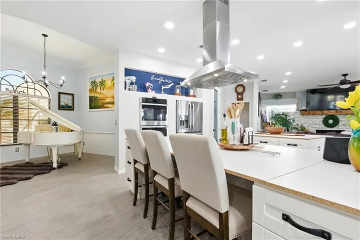 Kitchen featuring stainless steel appliances, crown molding, backsplash, white cabinets, and island range hood