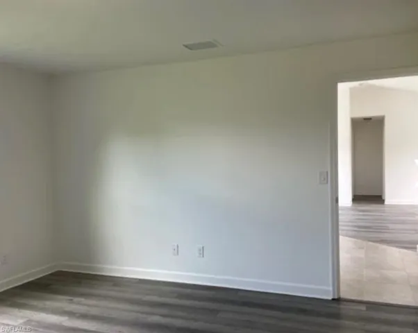 Empty room with dark wood-type flooring and baseboards