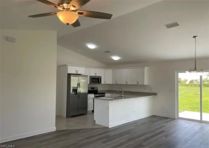 Kitchen with open floor plan, appliances with stainless steel finishes, white cabinetry, lofted ceiling, and dark wood-style floors