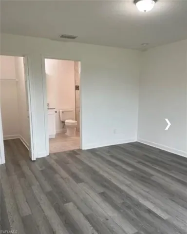 Unfurnished bedroom featuring a spacious closet, dark wood-type flooring, and ensuite bathroom