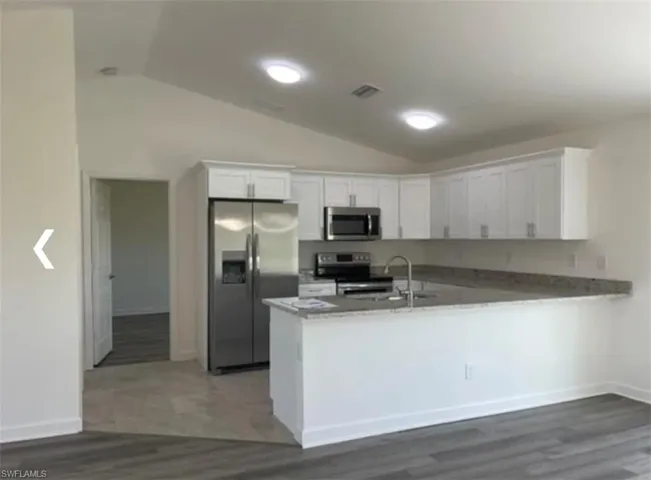 Kitchen with white cabinets, stainless steel appliances, lofted ceiling, dark wood-style floors, and a peninsula
