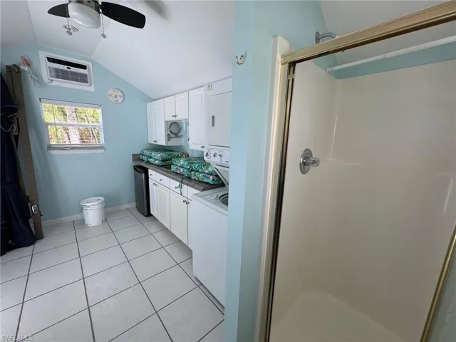 Bathroom featuring stacked washer / drying machine, walk in shower, lofted ceiling, ceiling fan, and vanity