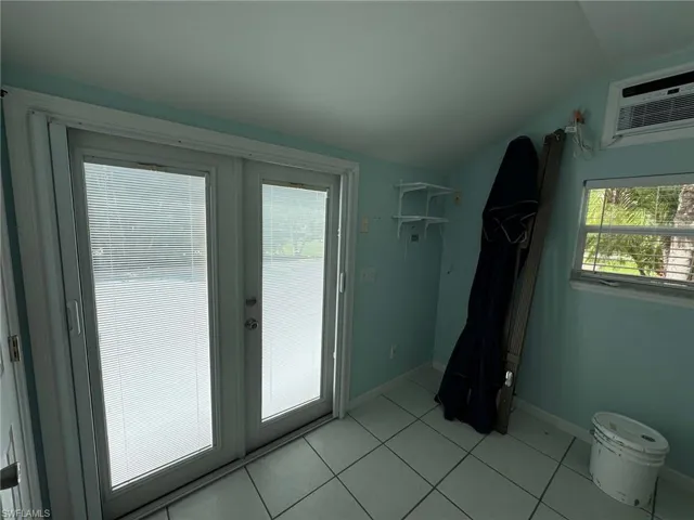 Doorway to outside with lofted ceiling, a wall mounted AC, and light tile patterned floors