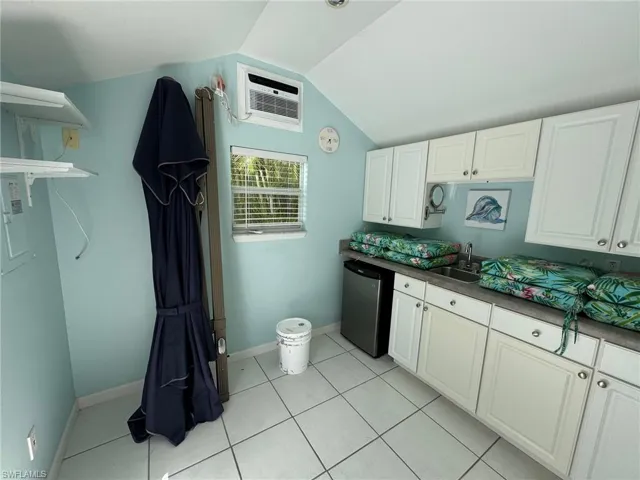 Kitchen featuring stainless steel dishwasher, vaulted ceiling, sink, and white cabinetry