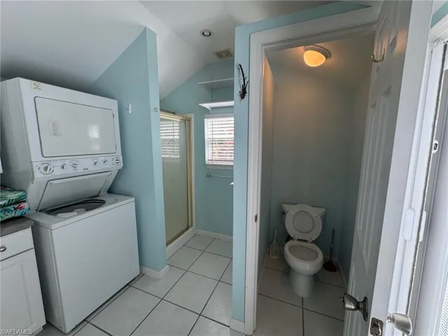 Clothes washing area with stacked washer and clothes dryer and light tile patterned floors