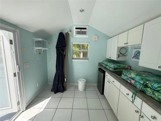 Kitchen with white cabinets, dishwasher, vaulted ceiling, a wall mounted air conditioner, and light tile patterned flooring
