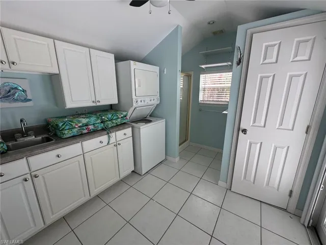 Kitchen with ceiling fan, sink, stacked washer / drying machine, and white cabinets