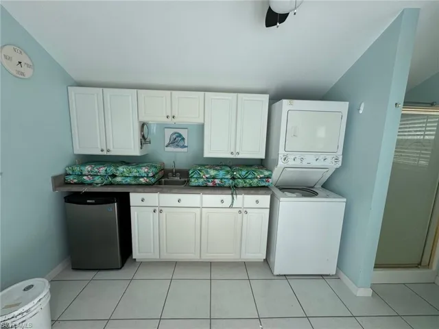 Kitchen featuring stainless steel refrigerator, light tile patterned floors, stacked washer and clothes dryer, ceiling fan, and white cabinets