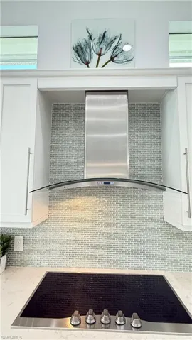 Cool modern glass exhas hood covers the cooktop and enhances the glass tile backsplash