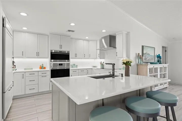 Kitchen with crown molding, lofted ceiling, visible vents, wall chimney range hood, and a kitchen bar