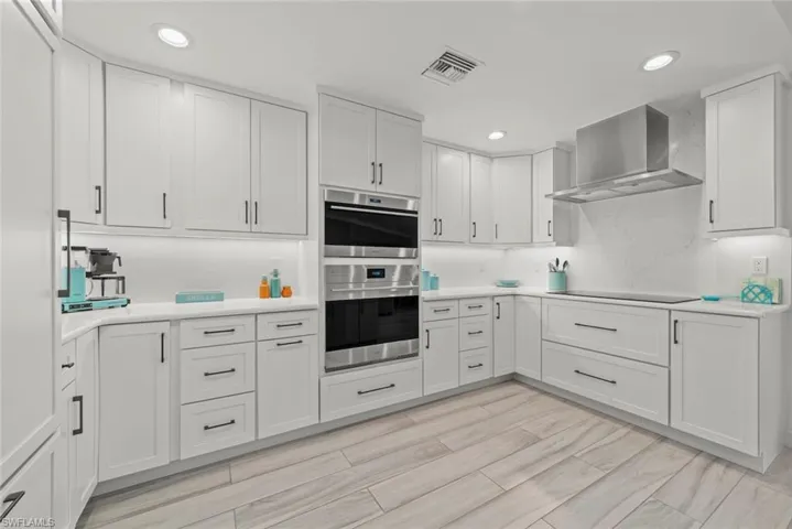 Kitchen with light countertops, wall chimney range hood, double oven, and visible vents