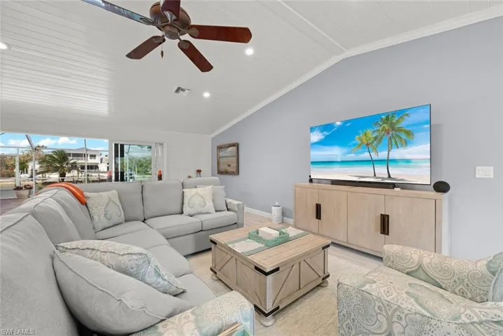 Living area with lofted ceiling, a ceiling fan, baseboards, visible vents, and crown molding