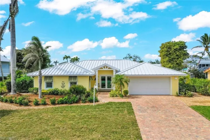 Ranch-style house featuring an attached garage, a standing seam roof, decorative driveway, french doors, and a front lawn