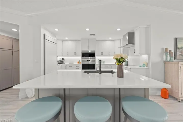 Kitchen with lofted ceiling, crown molding, wall chimney range hood, double oven, and a sink